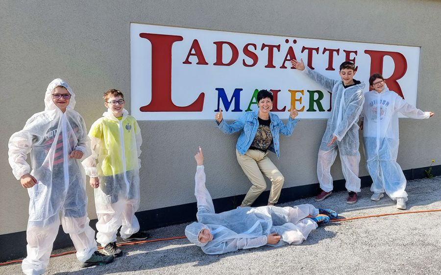 Kinder und Lehrerin in Schutzanzügen vor dem Firmenlogo von Ladstätter Malerei beim Berufsinfotag